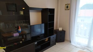 Un salon moderne doté d’un téléviseur à écran plat, d’un meuble de rangement noir, d’une petite table et d’une fenêtre avec des rideaux.