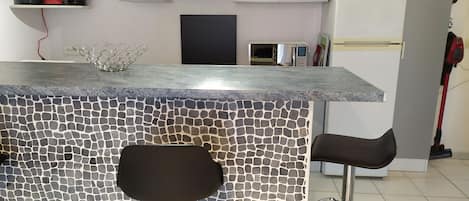 A kitchen with a stone backsplash, two bar stools, a coffee maker, and a microwave.