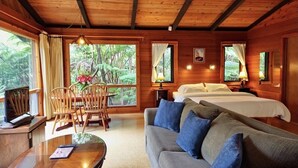 A wooden cabin interior with a sofa, two beds, a dining table, and chairs. - The Pacifica Inn/ The Gecko and Volcano Room (Volcano)