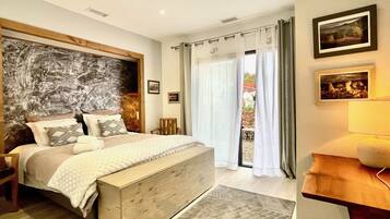 Een slaapkamer met een groot bed, een houten hoofdbord, een nachtkastje, een lamp en een uitzicht door het raam.