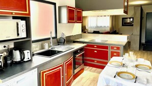A compact kitchen with a sink, stove, and a dining area set for four. - Les Terres Rouges du Salagou 5min du lac ! Natura 2000 , Atelier D'artiste (Le Bosc)