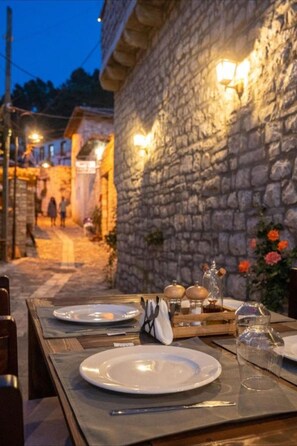 An outdoor dining area with stone walls and warm lighting, featuring tables set with plates and cutlery. - Bujtina Kapllani (Berat)