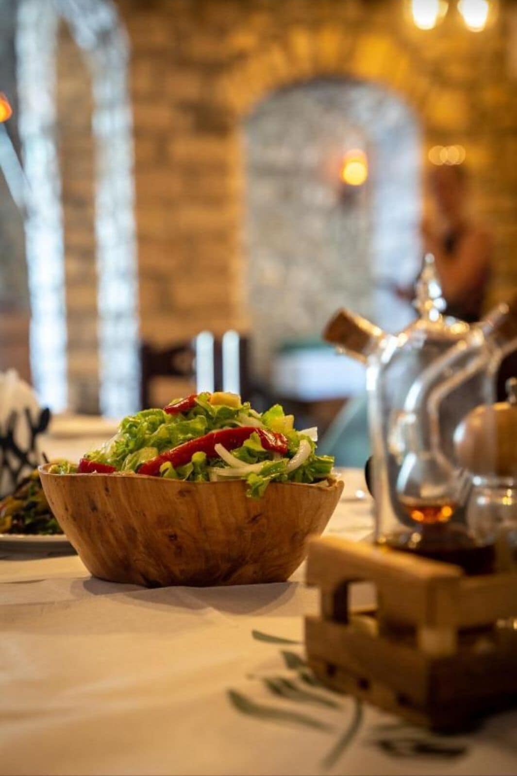 Eine Holzkugel mit Salat auf einem Tisch, im Hintergrund eine Glaskaraffe und eine Flasche.
