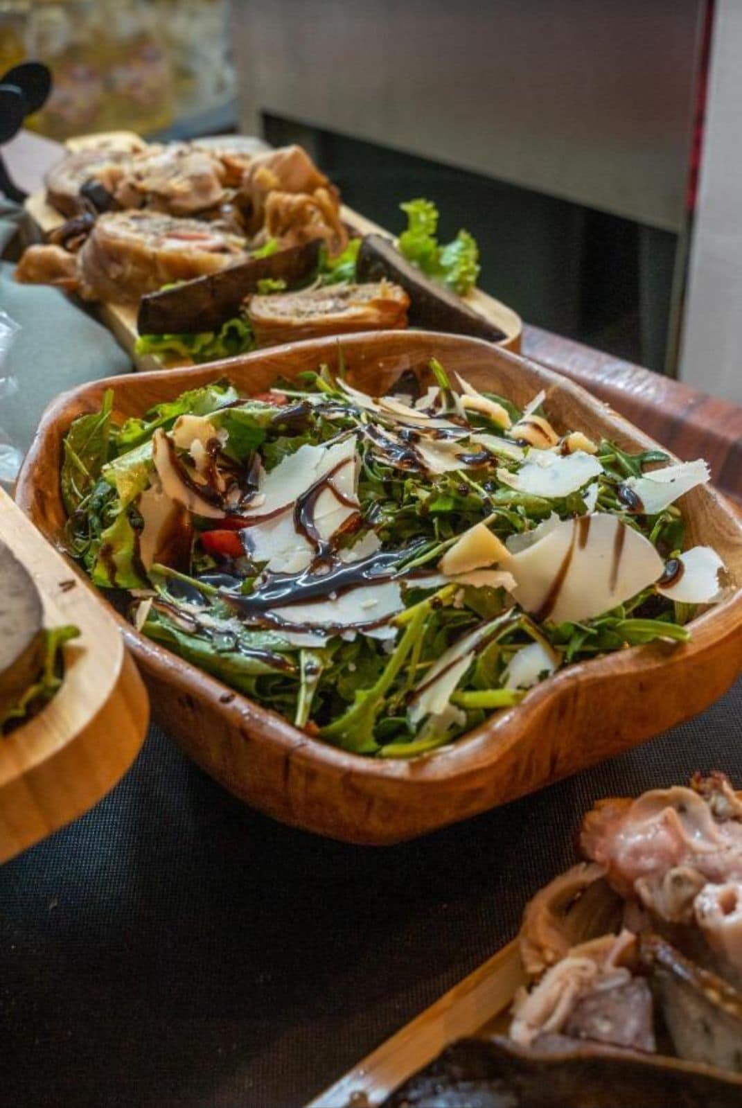 A wooden serving tray with a salad, including greens, cheese, and a dark dressing.