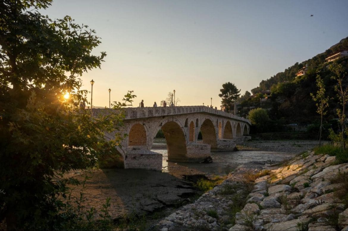 A stone bridge with arches over a river, surrounded by trees and hills.