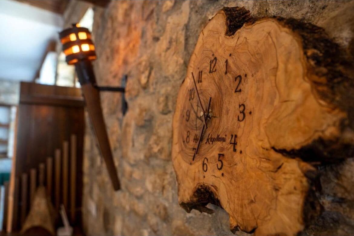 A wooden wall clock with Roman numerals and a candle holder.