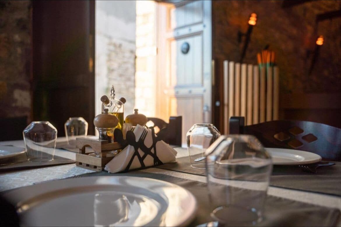 Una mesa de comedor dispuesta con platos, vasos y una botella de aceite de oliva.