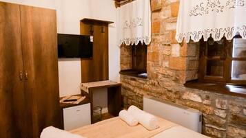 Un dormitorio con un armario de madera, un televisor de pantalla plana, una pared de piedra y una ventana con cortinas.