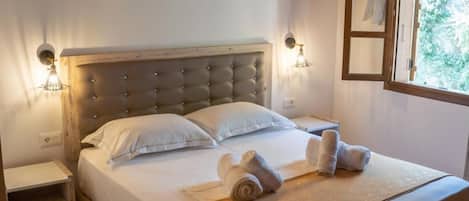 Ein ordentlich bezogenes Bett mit einer gebügelten Kopfstütze, zwei Nachttischlampen und gerollten Handtüchern auf dem Bett.