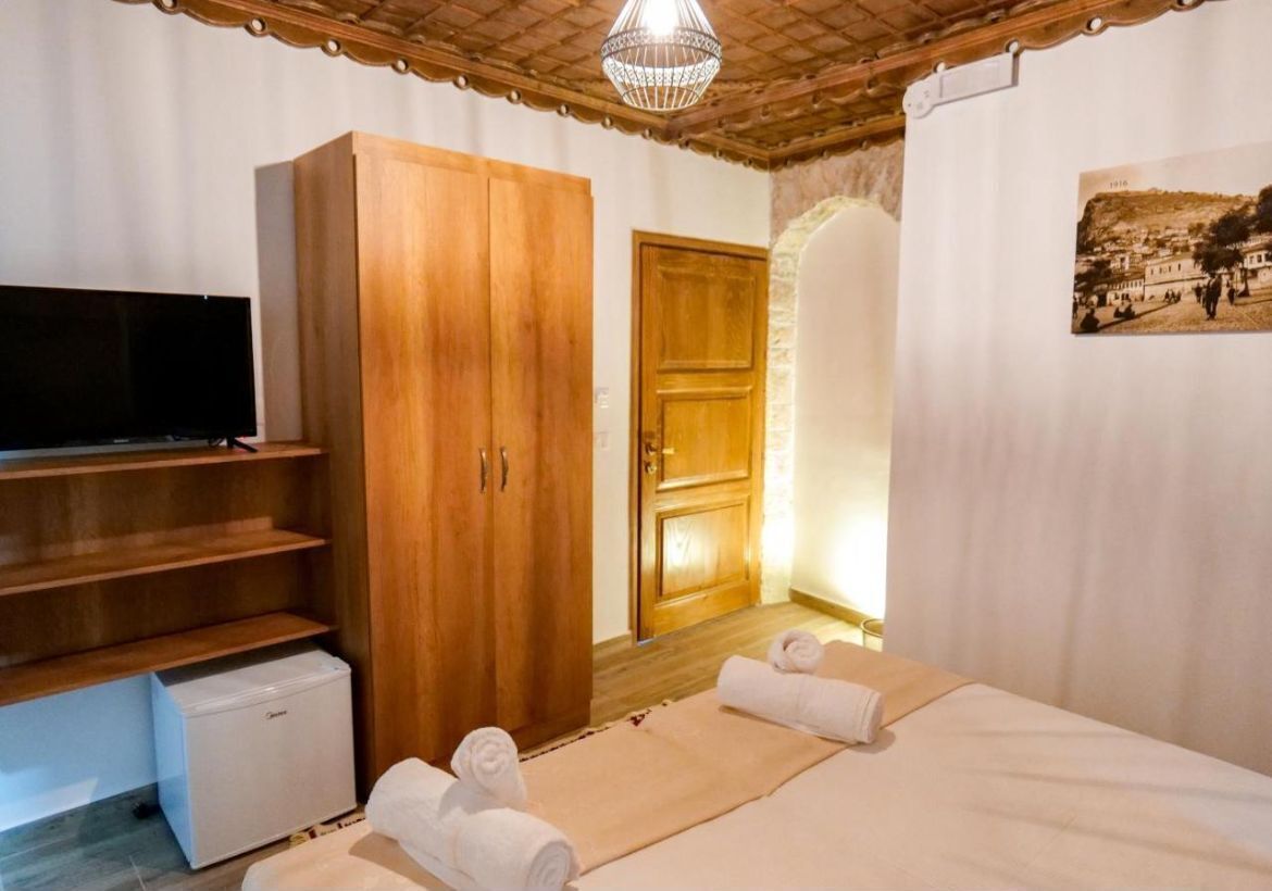 Habitación de hotel con armario de madera, televisor, refrigerador pequeño, cama con toallas y un cuadro en la pared.