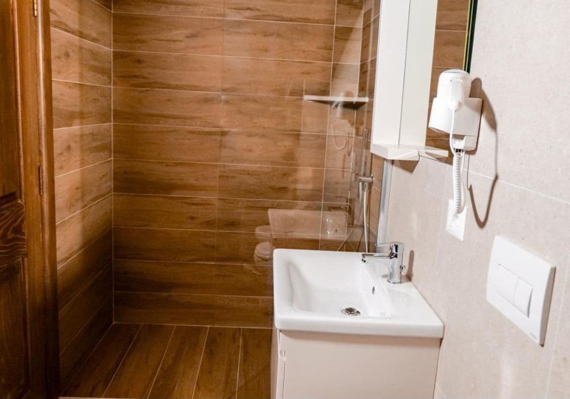Ein Badezimmer mit Holzboden, Waschbecken in Weiß und einem Spiegel.