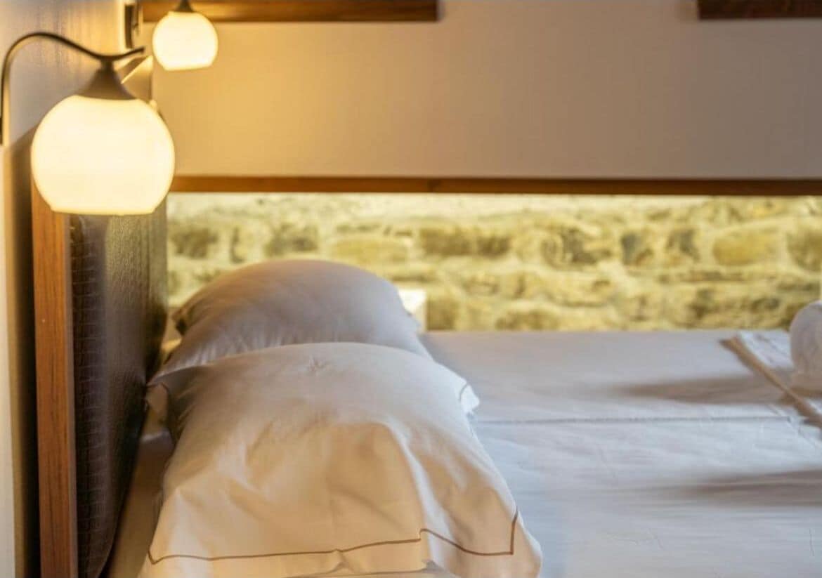 A bed with white linens and a stone wall in the background.