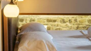 A bed with white linens and a stone wall in the background.
