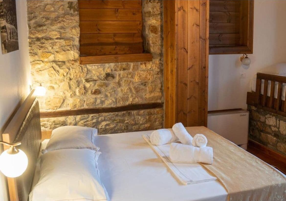 A cozy room with a stone wall, wooden beams, a bed with white linens, and a small table with towels.