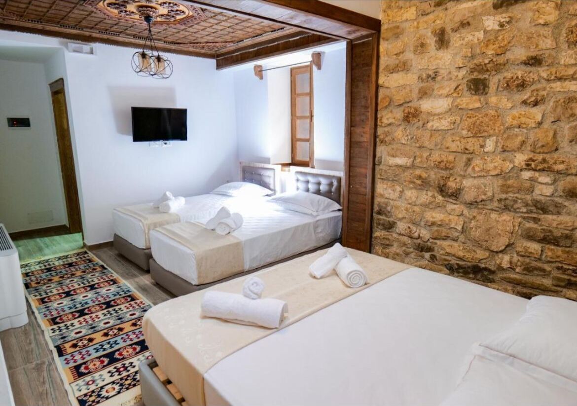 Un dormitorio con dos camas, una pared de piedra, un televisor y una alfombra estampada.
