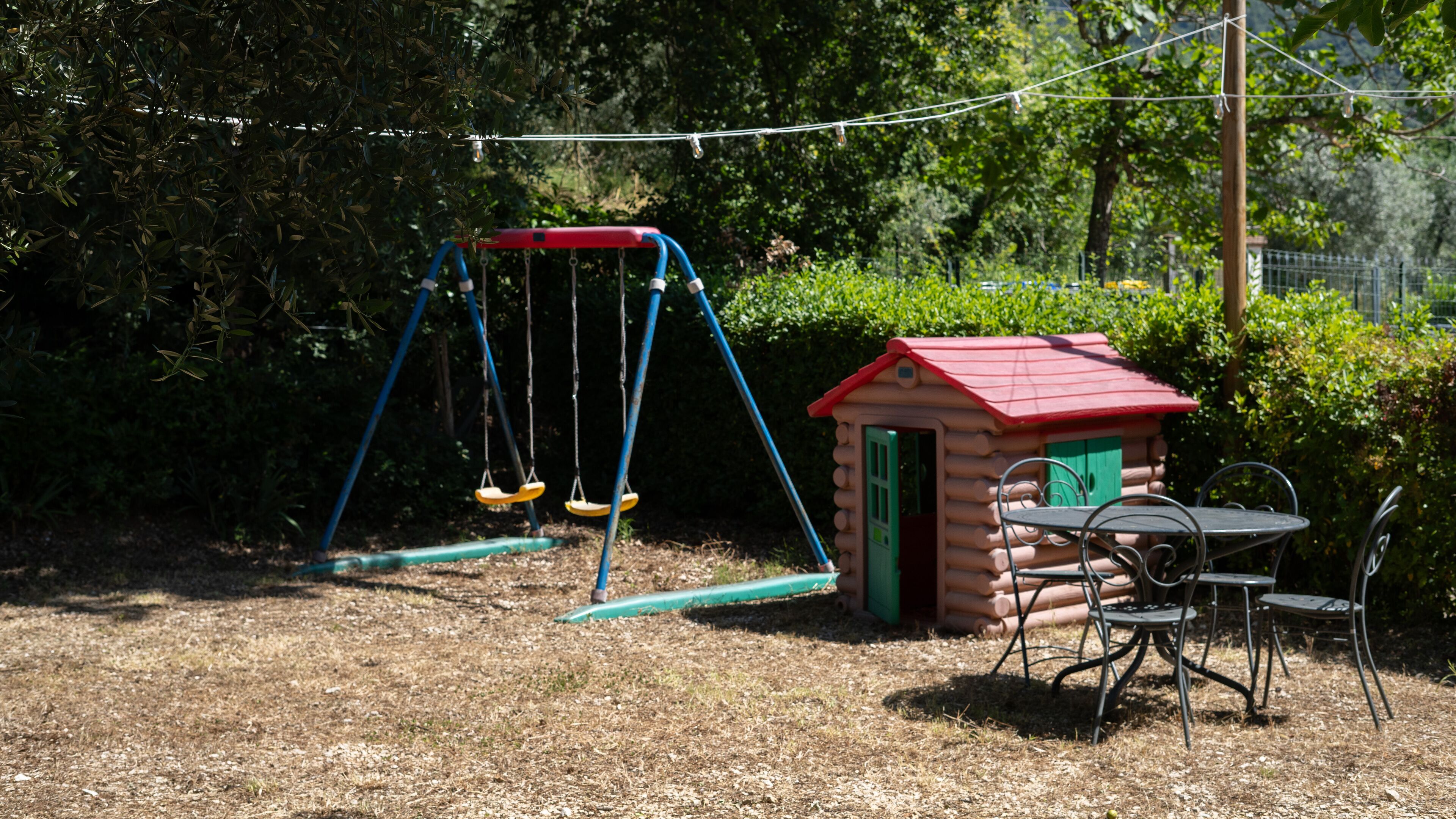 A playground with swings and a small shed, surrounded by trees and a grassy area.