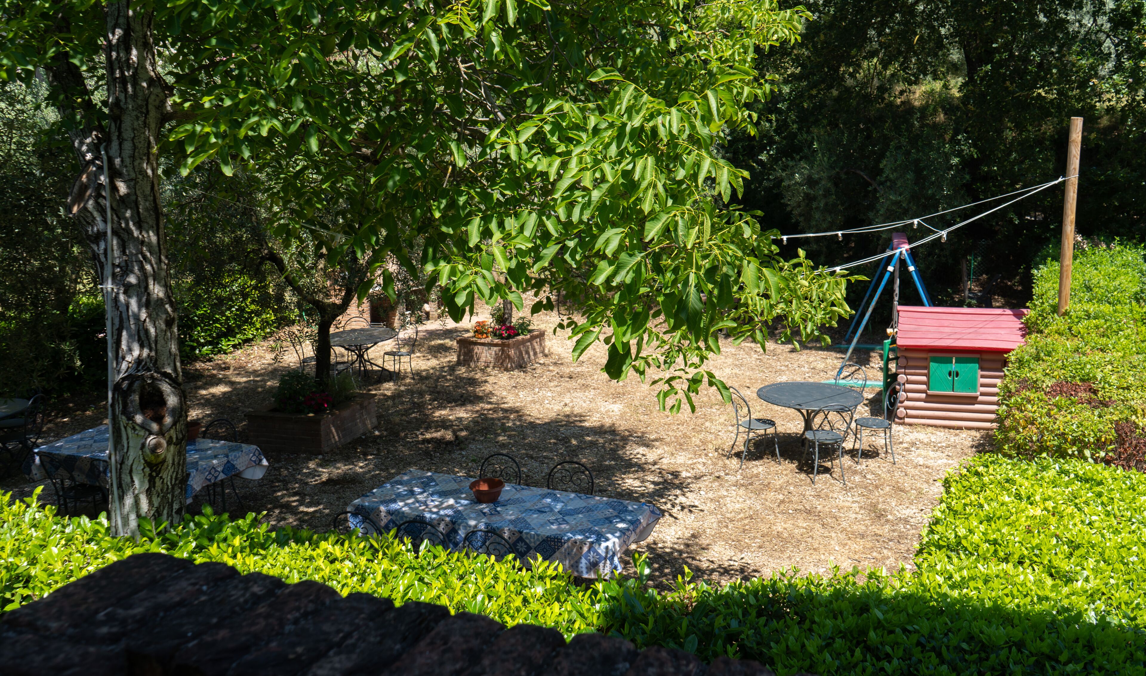 Ein Garten mit Tisch und Stühlen unter einem Baum, einer Schaukel und einem kleinen Gartenhaus.