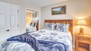 Ein Schlafzimmer mit Bett, Nachttisch, Lampe, Spiegel und einem Bild an der Wand.