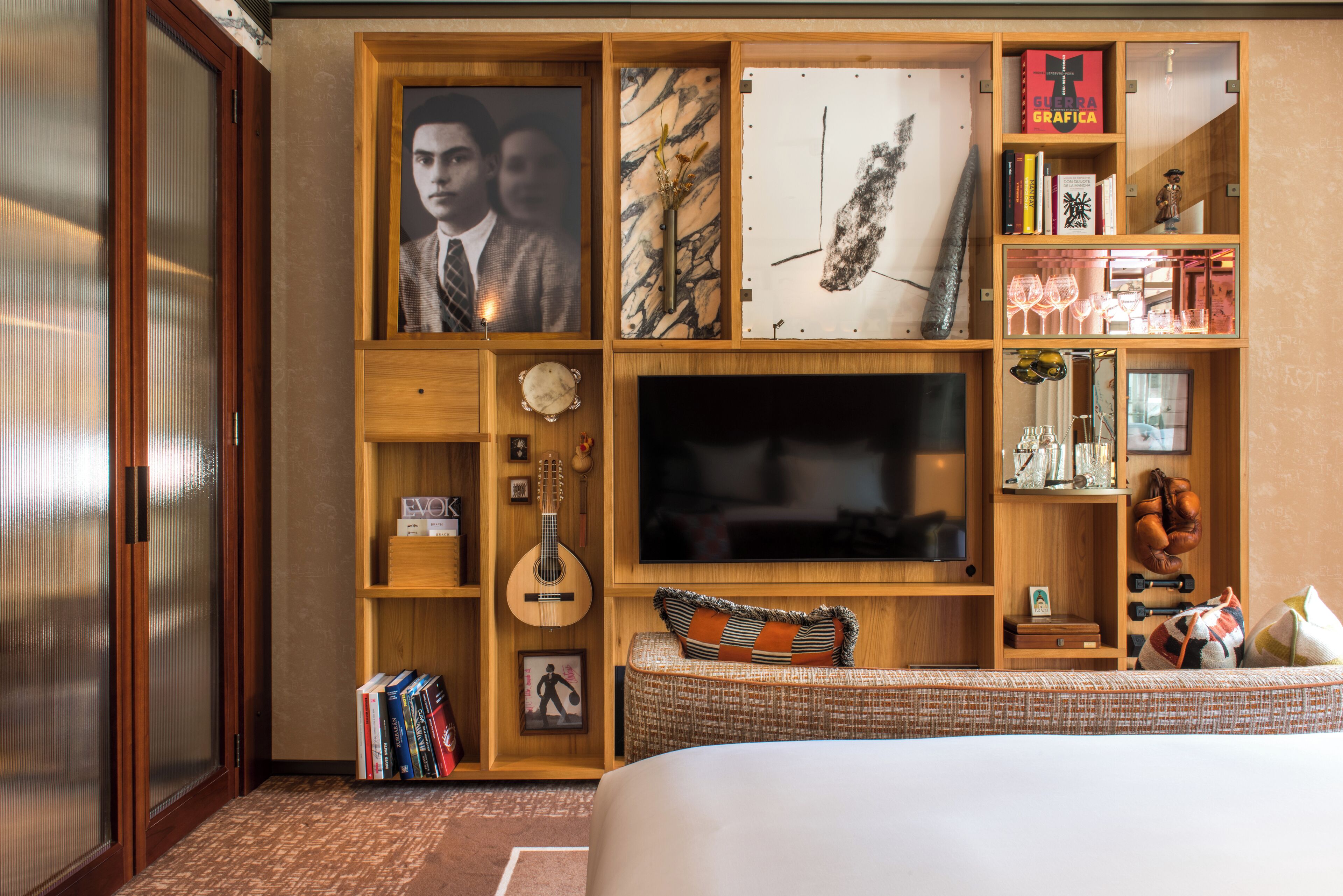 A bedroom with a large bed, a television, a wooden bookshelf, and various decorative items.