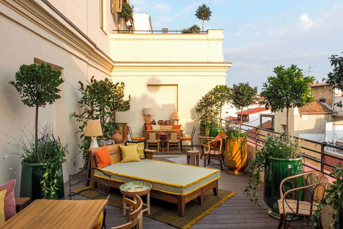A rooftop terrace with a sofa set, dining table, chairs, and potted plants.