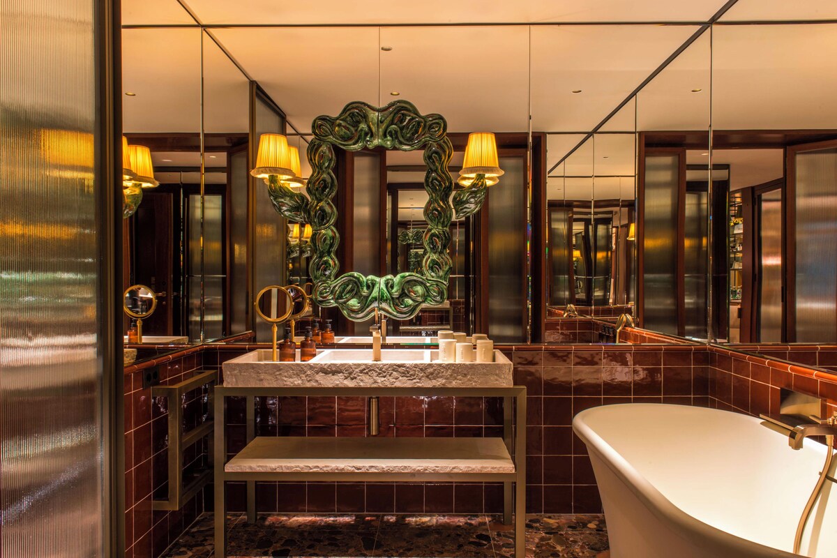 A modern bathroom with a freestanding bathtub, a large mirror with ornate detailing, and a vanity with a marble countertop.