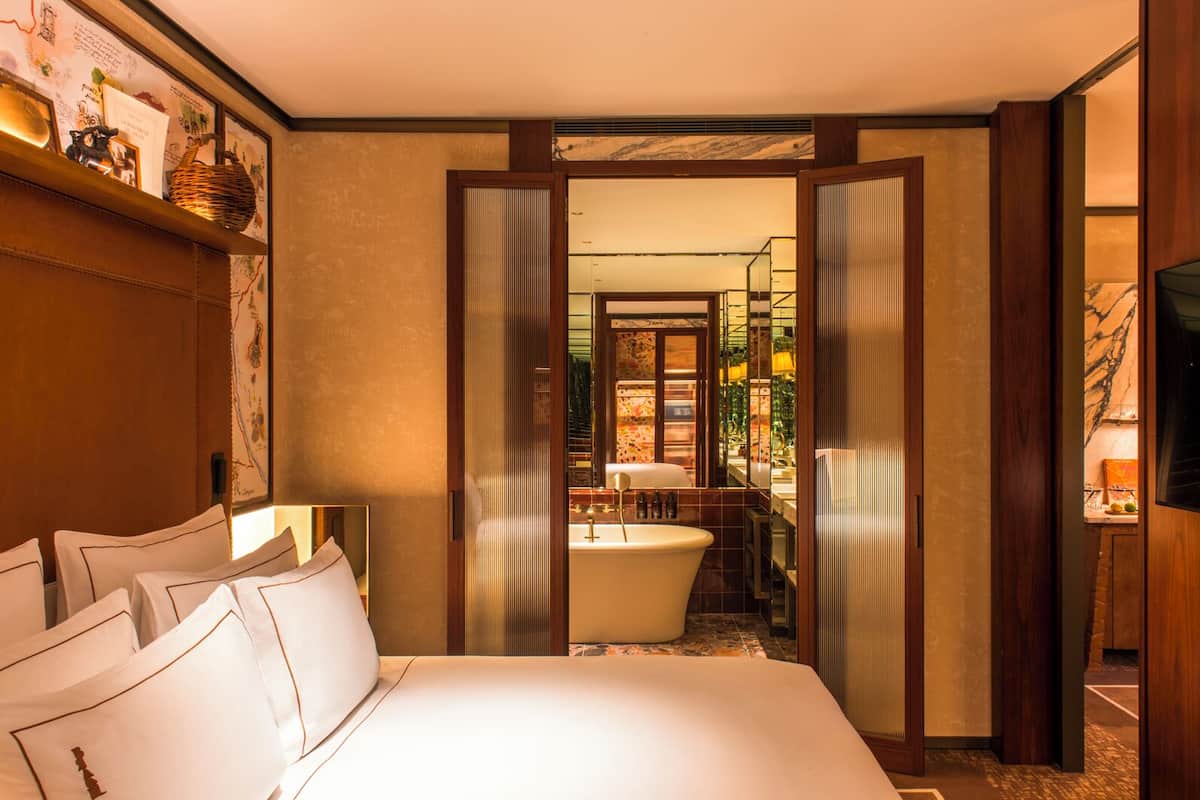 A hotel room with a large bed, a vanity with a bathtub, and a television.
