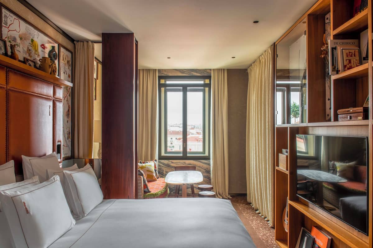 A hotel room with a large bed, a small table, a TV, and a window with curtains.