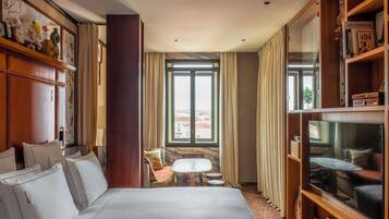 Habitación de hotel con una cama grande, una mesita pequeña, un televisor y una ventana con cortinas.