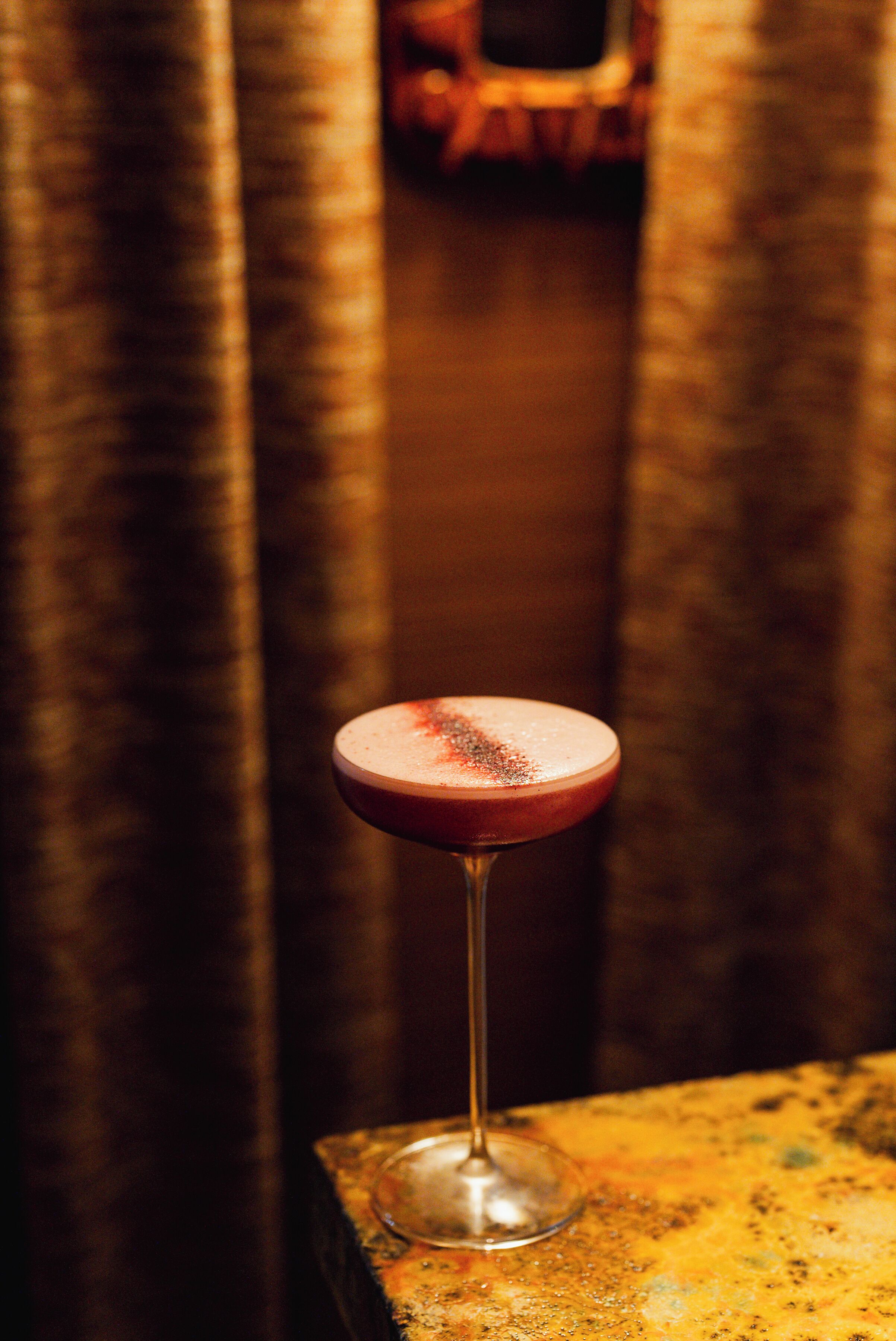 Un cocktail servi dans un verre à pied, posé sur une surface texturée.