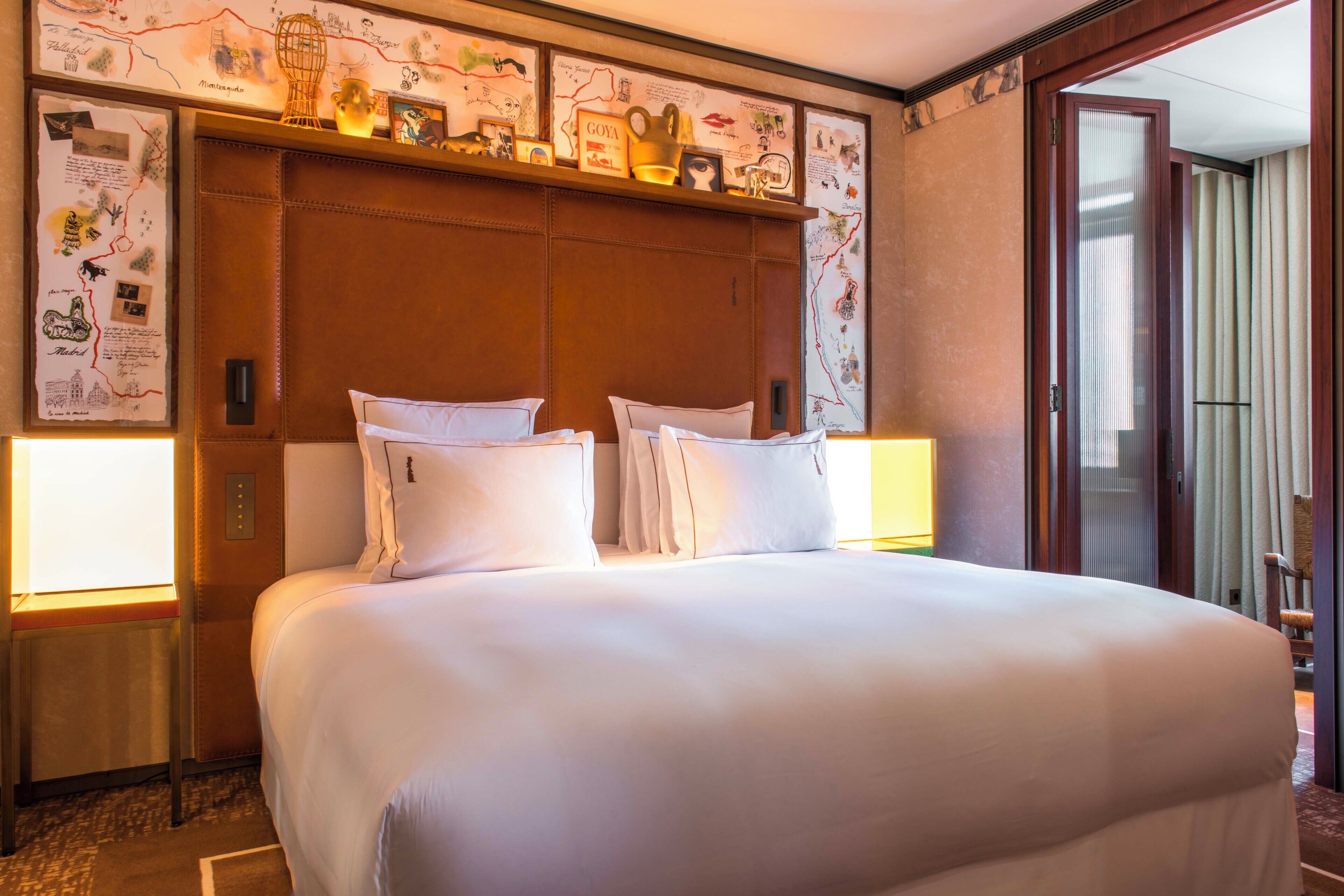 A hotel room with a large bed, two bedside tables, a wooden headboard, and wall decor including maps and framed pictures.
