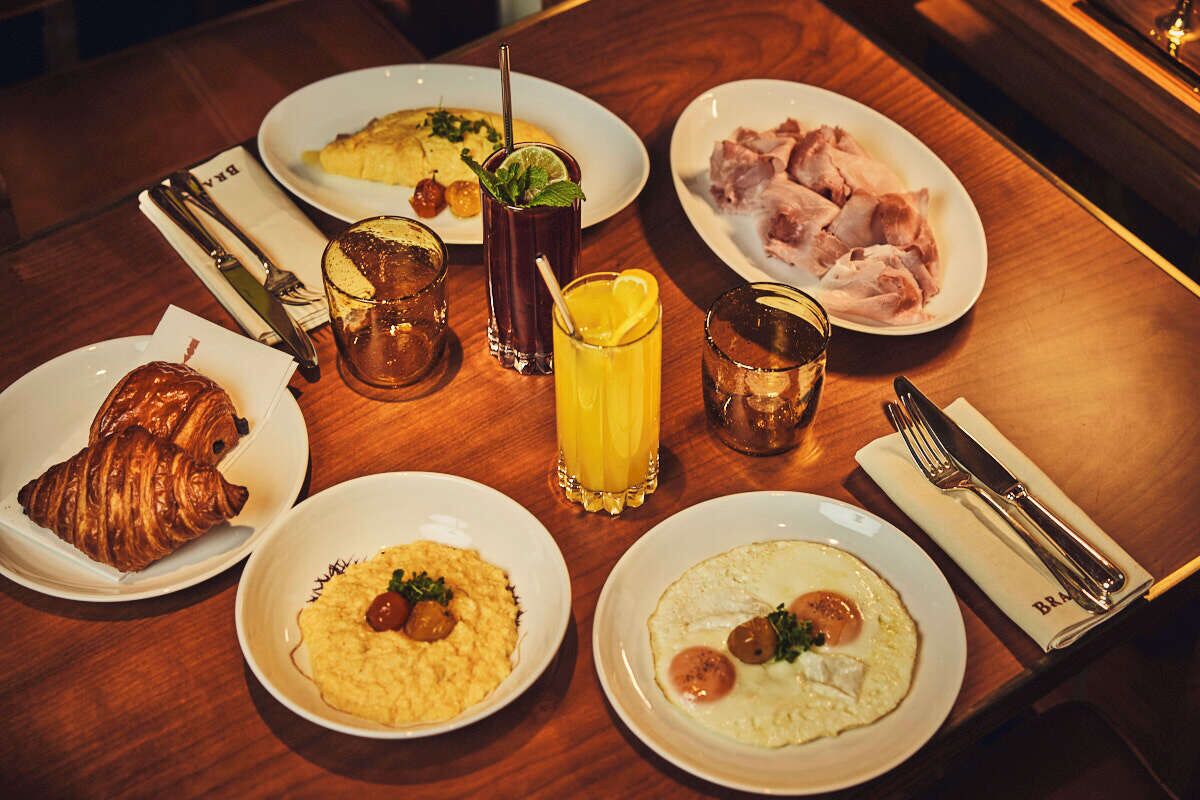 Una escena de desayuno con platos de comida, bebidas y cubiertos sobre una mesa de madera.