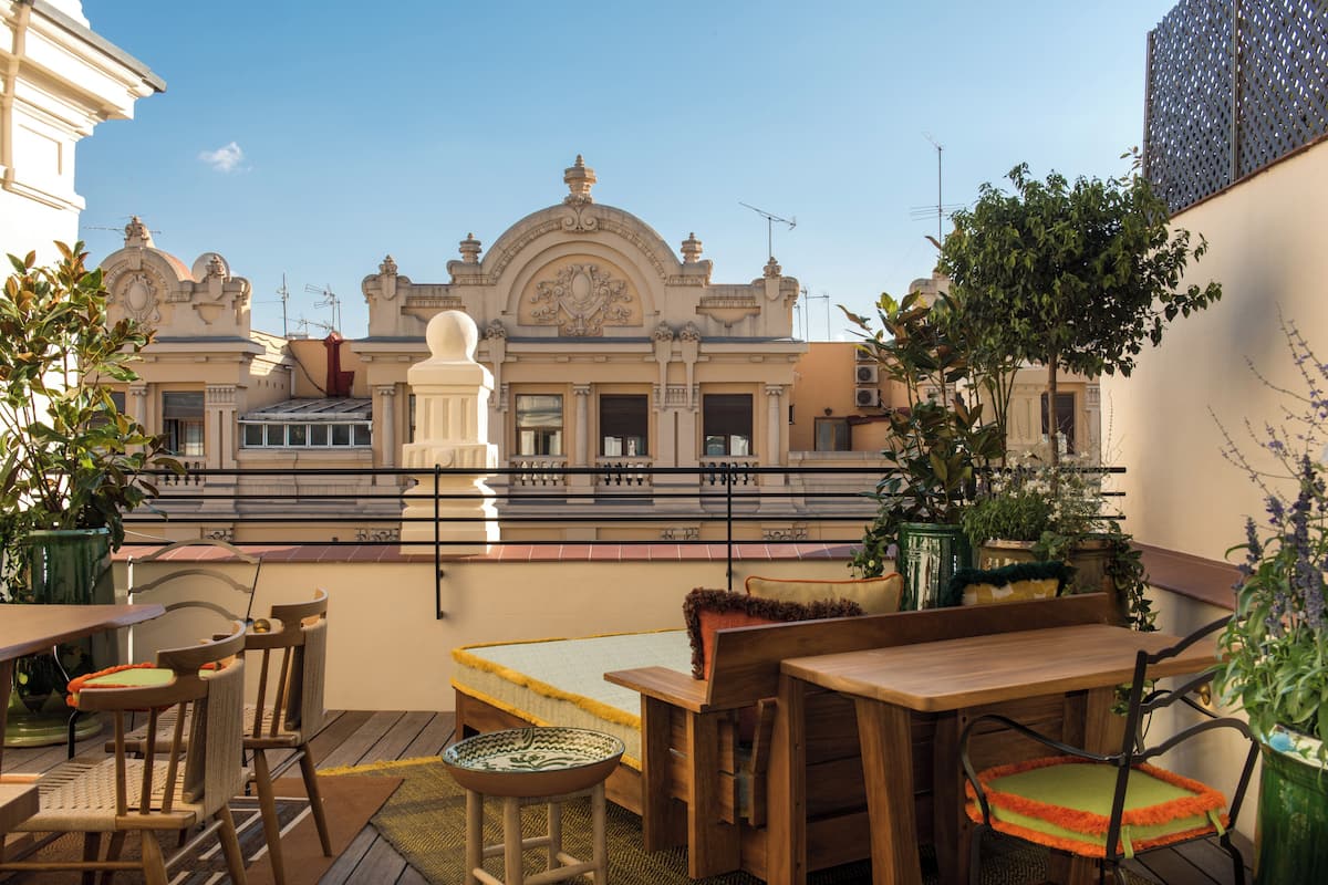 An outdoor terrace with wooden furniture, potted plants, and a view of a historic building with ornate architecture.