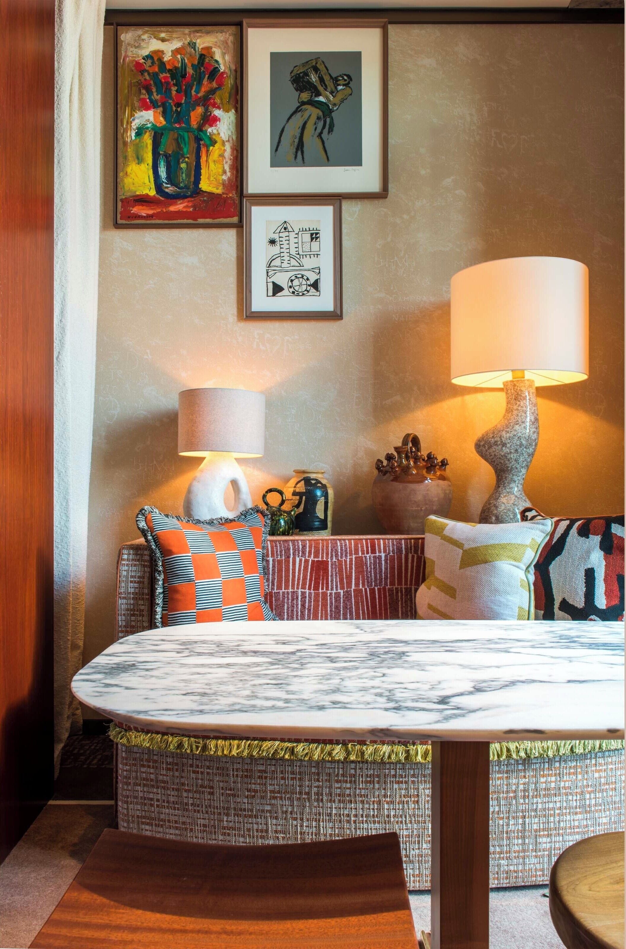 A cozy living room with a round coffee table, a sofa with patterned cushions, and a wall adorned with framed artwork.
