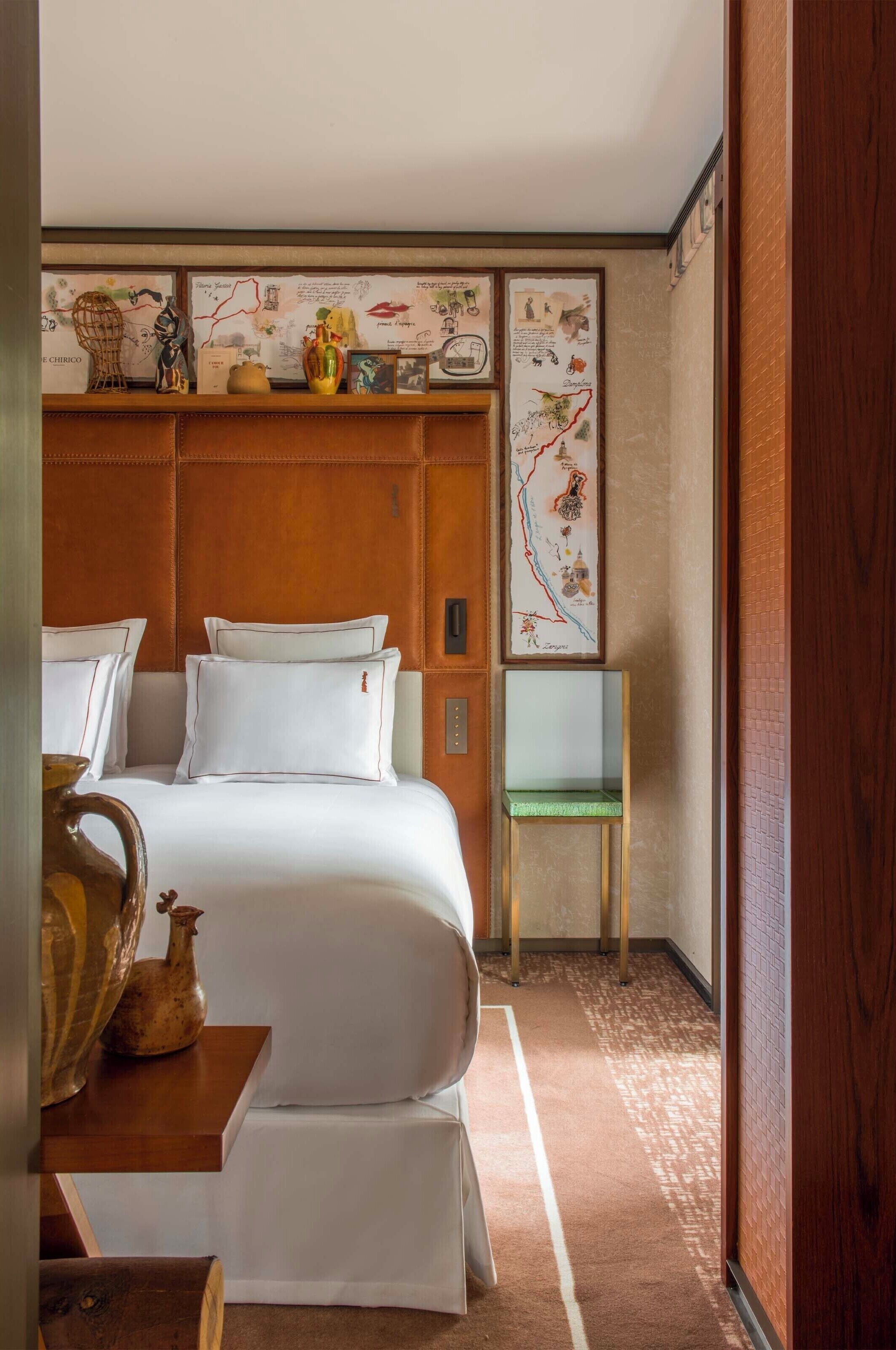 A hotel room with a large bed, a wooden headboard, a small table with a vase, and a decorative wall panel.