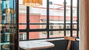 Una habitación de esquina con un ventanal grande, una silla de madera, una mesita y un candelabro.