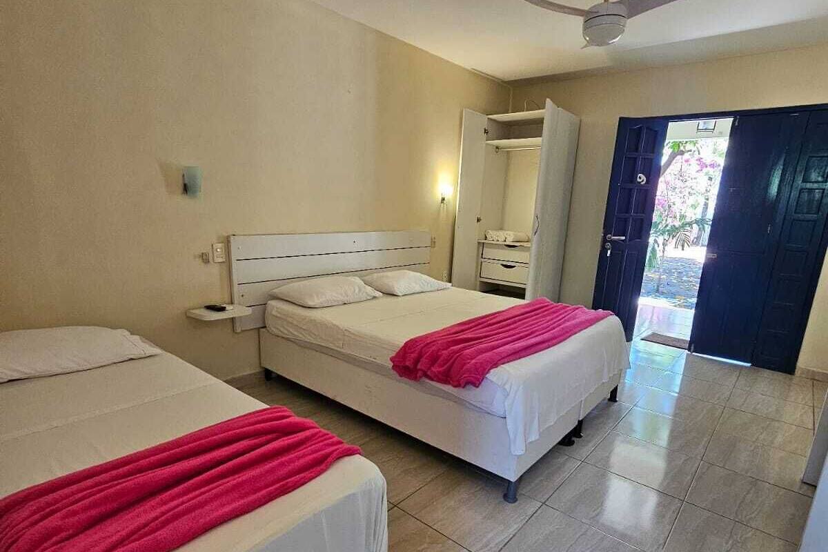 Habitación de hotel con dos camas, ventilador de techo, espejo y puerta que da a un balcón.