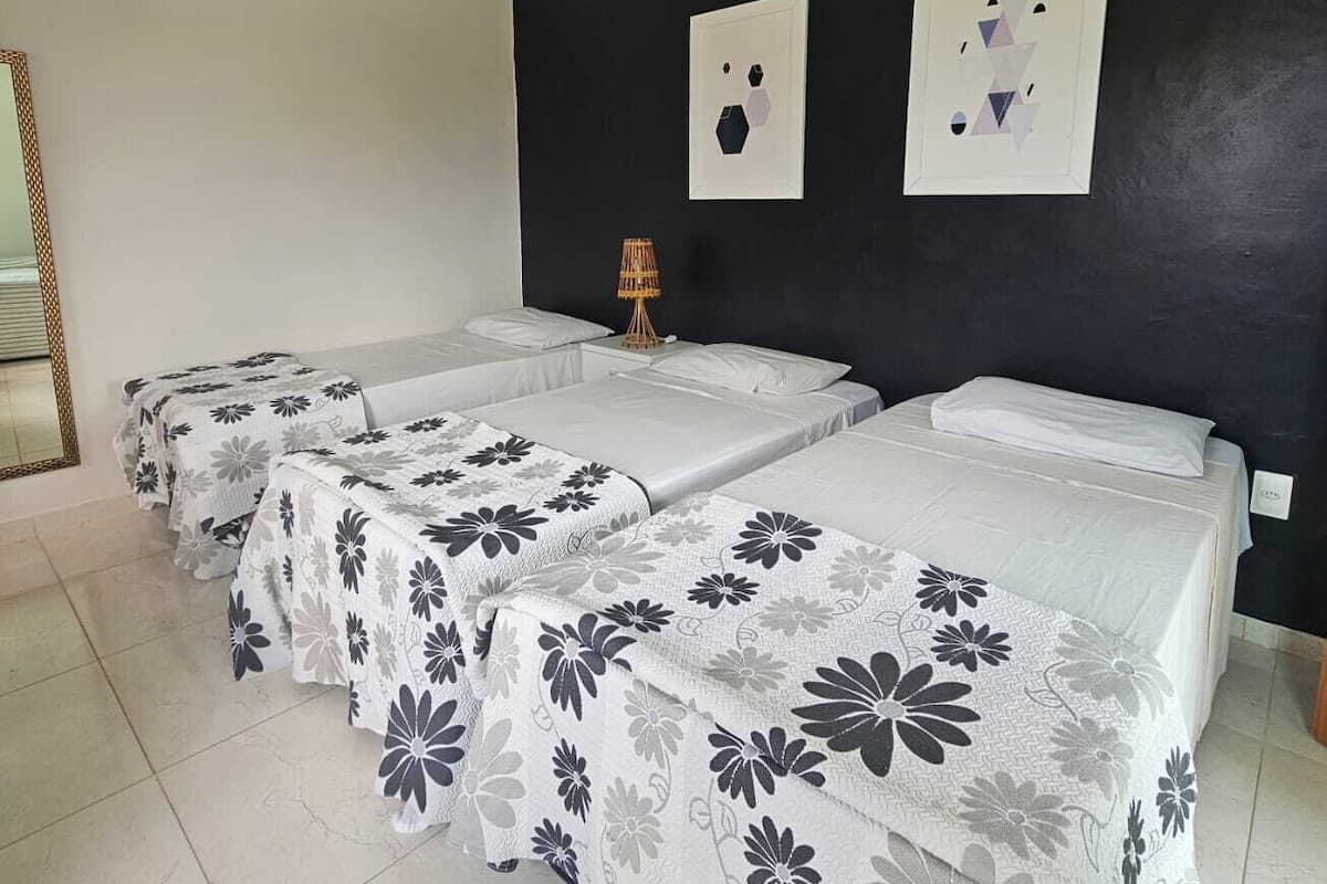 Habitación de hotel con tres camas, cada una con cubrecama estampado con motivos florales. Hay una lámpara de pared entre las camas y dos obras de arte enmarcadas encima de ellas.
