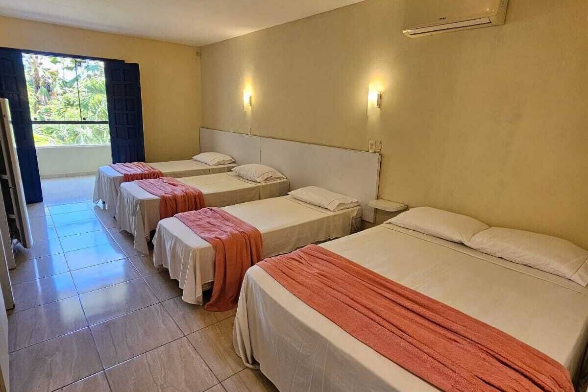 Habitación de hotel con tres camas, ventilador de techo y vistas al exterior.