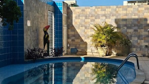 Una piscina con un muro de piedra y un edificio azulado en el fondo.