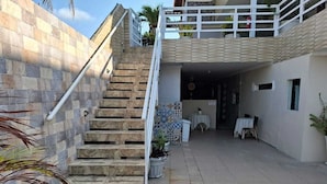 Una escalera conduce a un espacio exterior cubierto, con barandilla blanca, plantas en macetas y una mesa con sillas.