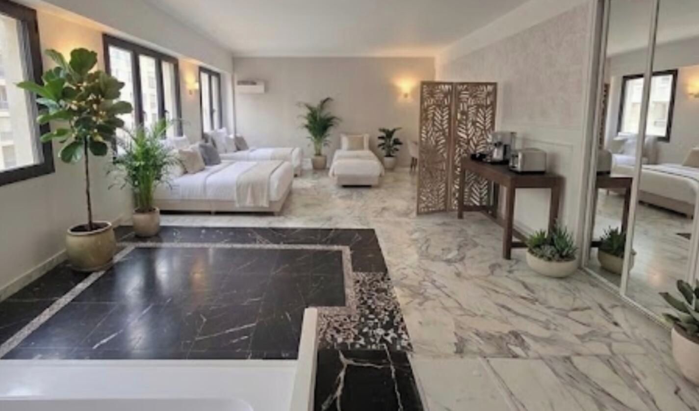 Une chambre d’hôtel avec un grand lit, un coin salon, une salle de bain avec baignoire et un miroir.
