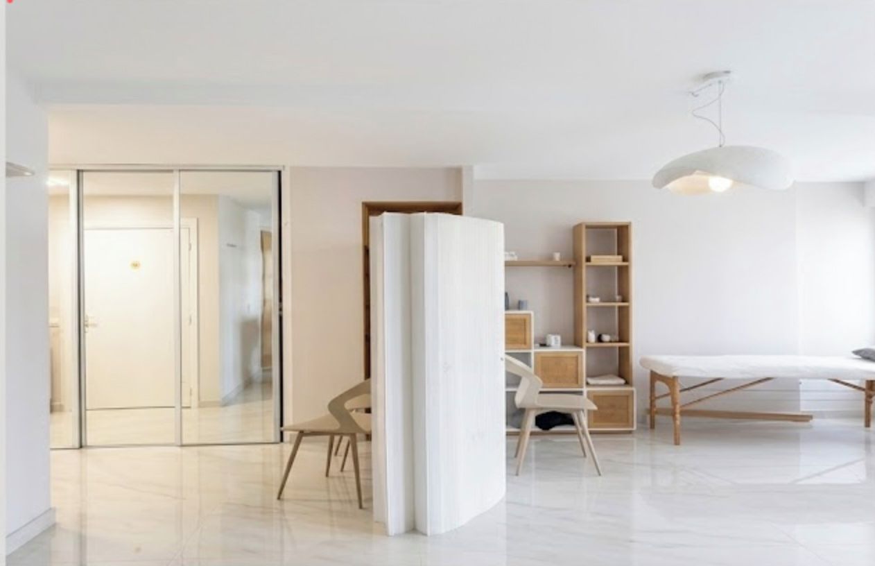 A modern interior with a glass door leading to a hallway, a wooden cabinet, a white bench, and a hanging light fixture.