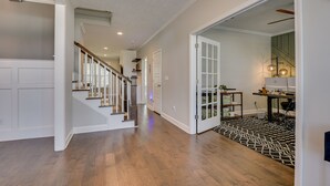 A spacious hallway with wooden flooring, a staircase, and a door leading to a room with a desk and computer. - Spacious 5BR Masters Retreat: Heated Pool/Spa, Theater, Basketball Court & More! (Evans)
