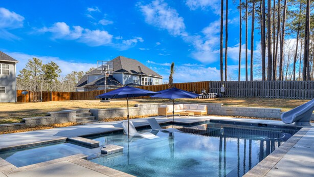 A swimming pool with a wooden deck, lounge chairs, and umbrellas. - Spacious 5BR Masters Retreat: Heated Pool/Spa, Theater, Basketball Court & More! (Evans)