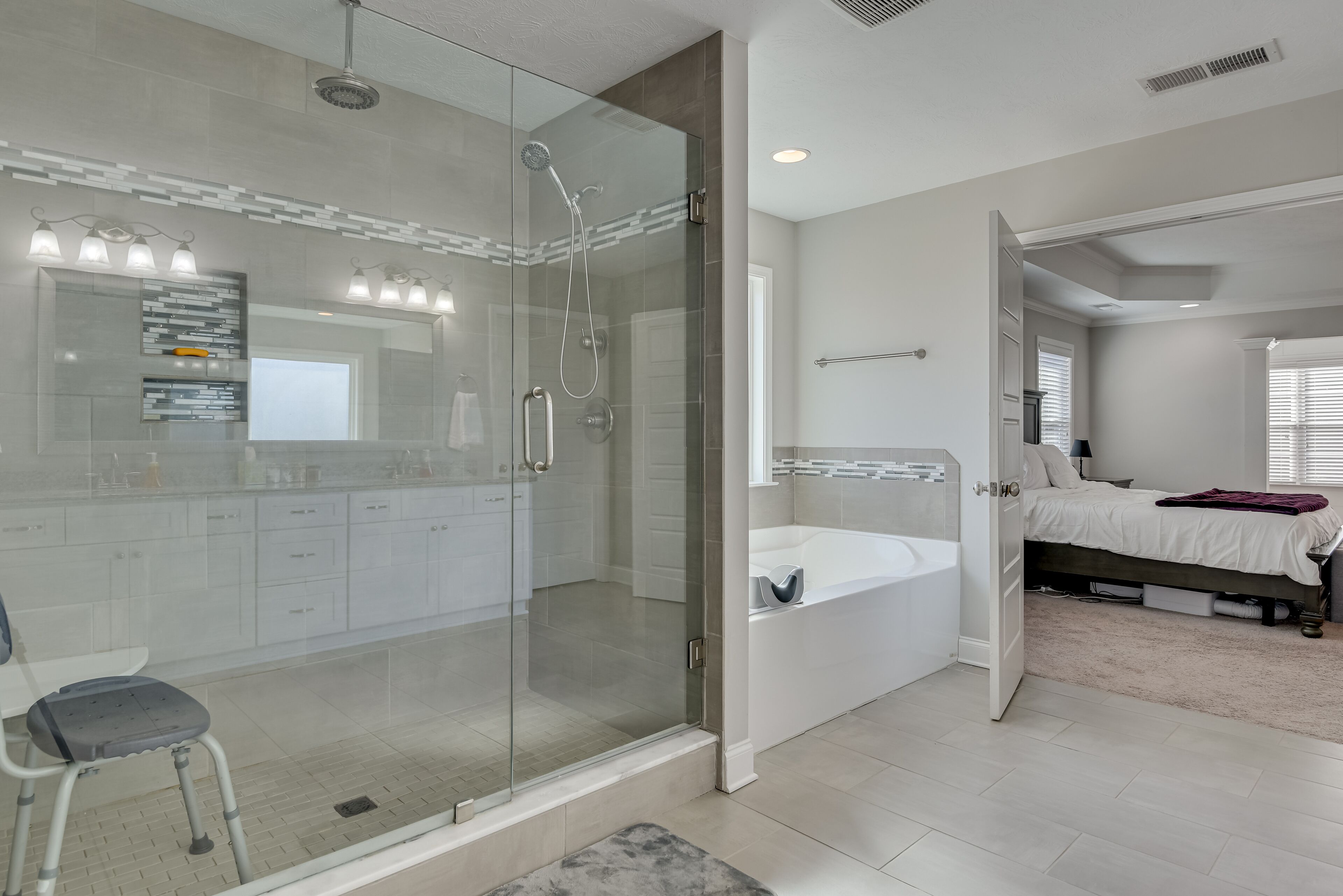 A modern bathroom with a glass-enclosed shower, a large mirror, and a white bathtub.