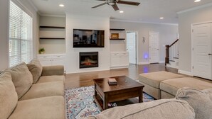 A modern living room with a fireplace, a ceiling fan, and a television mounted on the wall. - Spacious 5BR Masters Retreat: Heated Pool/Spa, Theater, Basketball Court & More! (Evans)