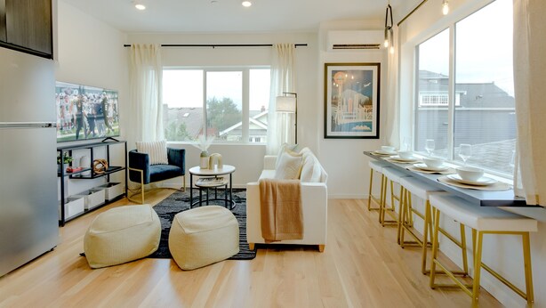 A modern living room with a sofa, ottoman, and a dining area with a long table. - Seattle Charm|Near University|3 BR|W&D|WIFI (Seattle)