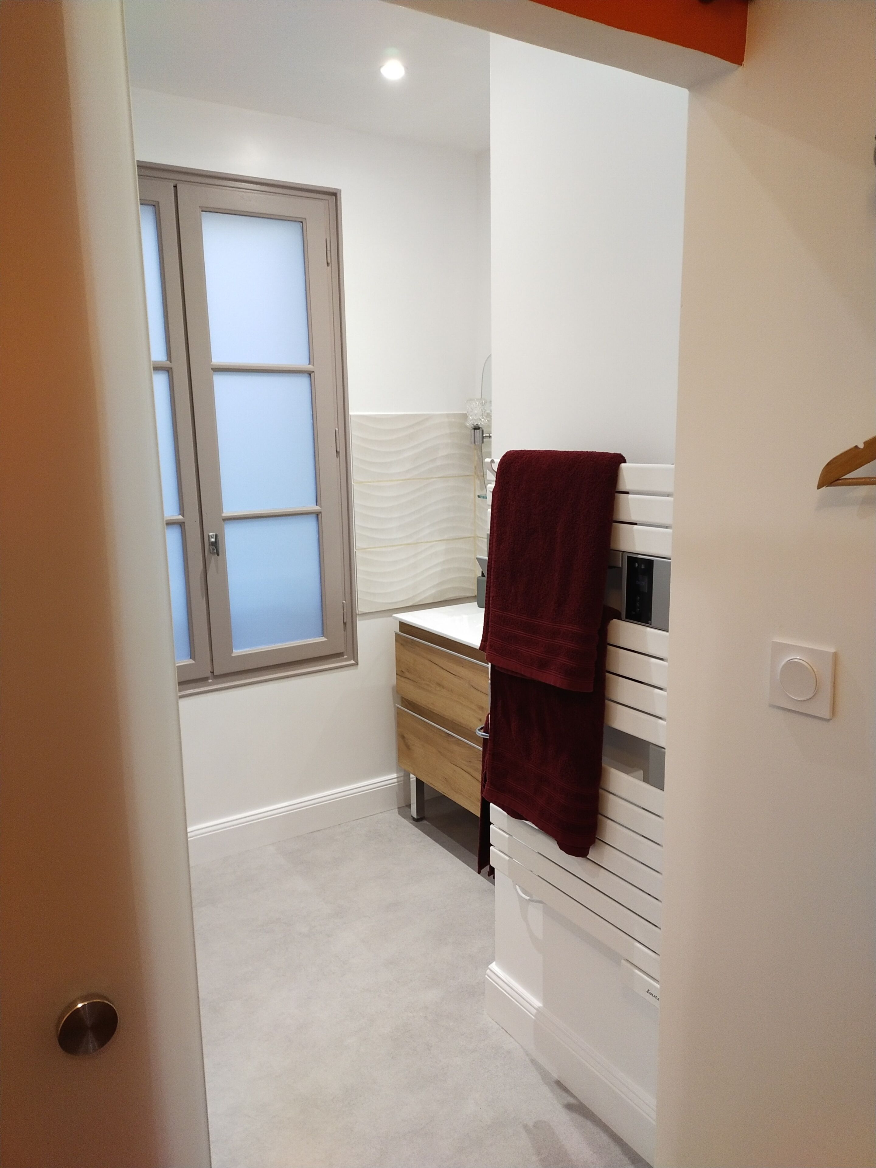 A compact bathroom with a white vanity, a towel hanging on the wall, and a frosted window.