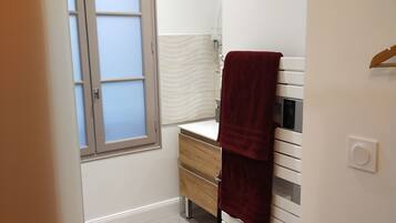 A compact bathroom with a white vanity, a towel hanging on the wall, and a frosted window.