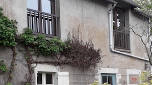 A two-story house with a balcony, a small garden with various plants and flowers, and a blue door.